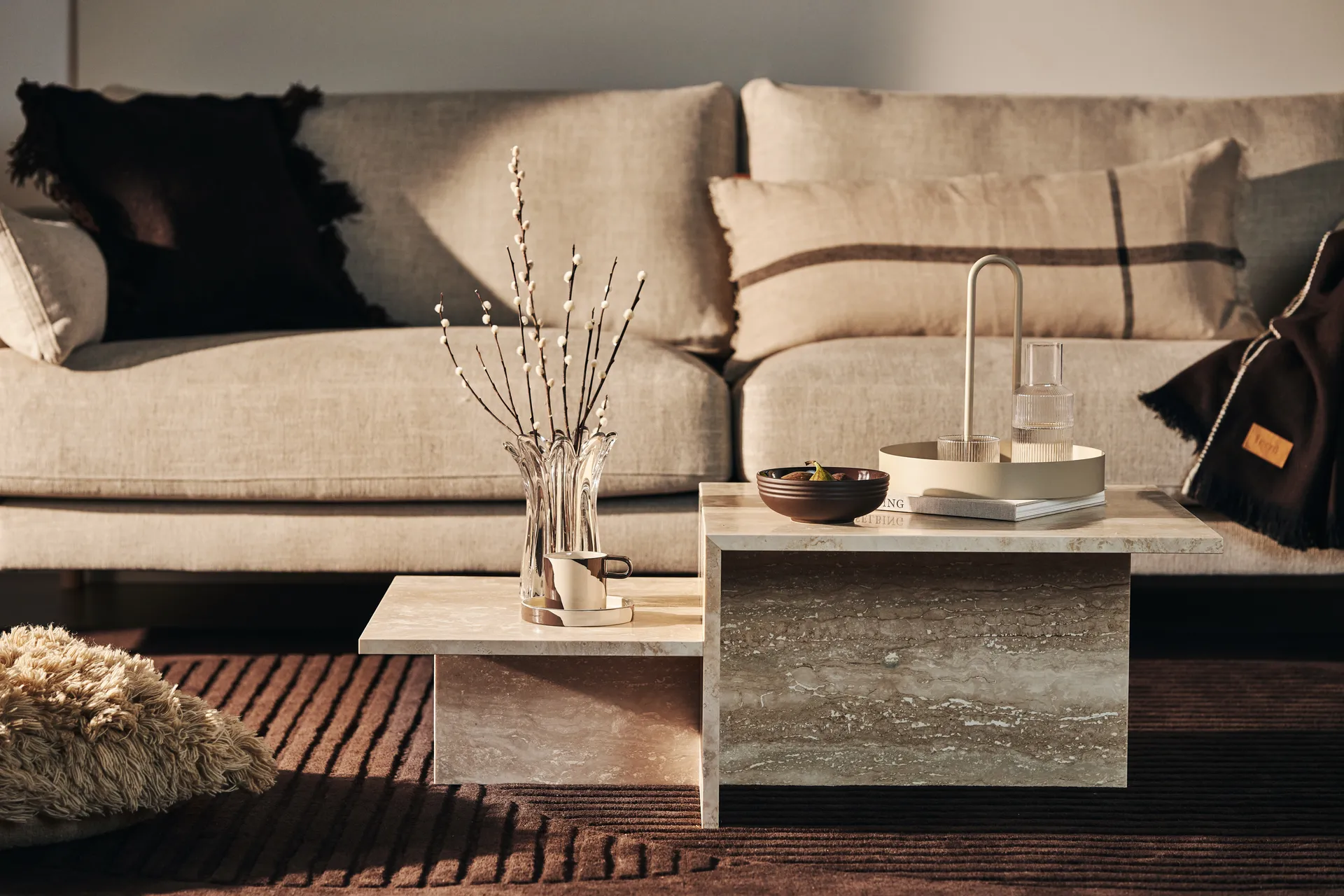 Tiered beige stone coffee tables in a living room with a neutral sofa and decorative accessories.