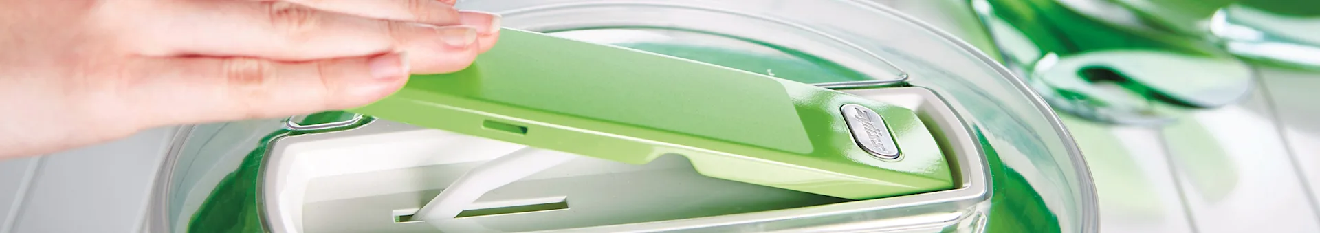Hand placing green lid with silver button onto a clear kitchen appliance.