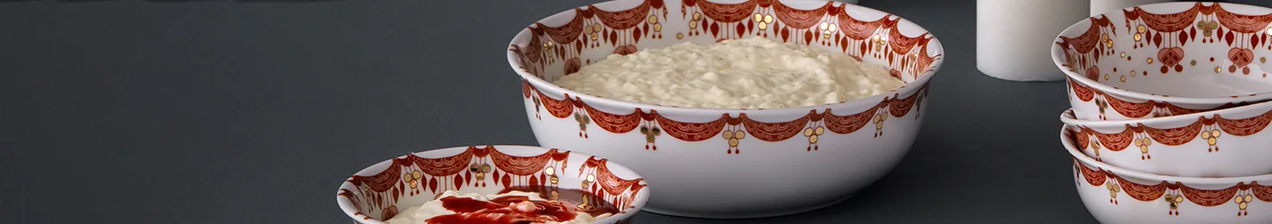 White patterned bowls, one large with rice pudding, one small with rice pudding and red sauce, and a stack of empty ones.