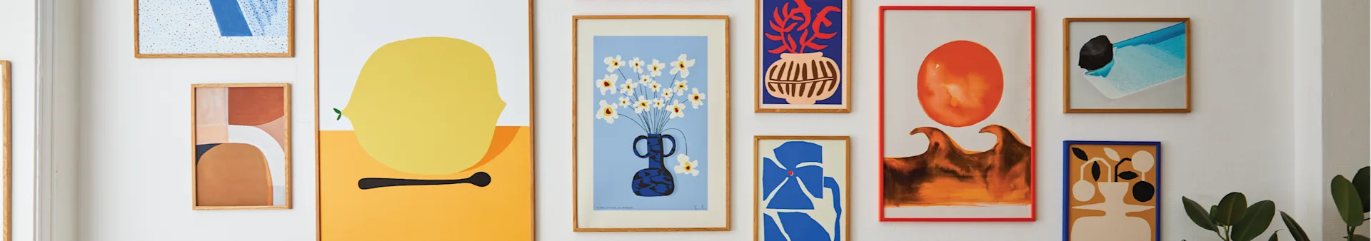 A gallery wall displaying several abstract art prints in various colors and styles, including a yellow lemon, flowers in a vase, and geometric shapes.
