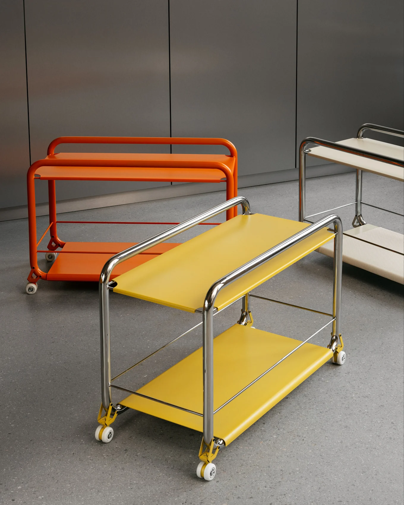 Three modern, two-tiered rolling carts: yellow with chrome, orange, and beige with chrome, on a grey floor.