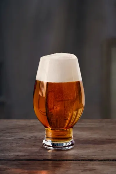 Tulip-shaped glass of amber beer with a thick white head on a rustic wooden table.