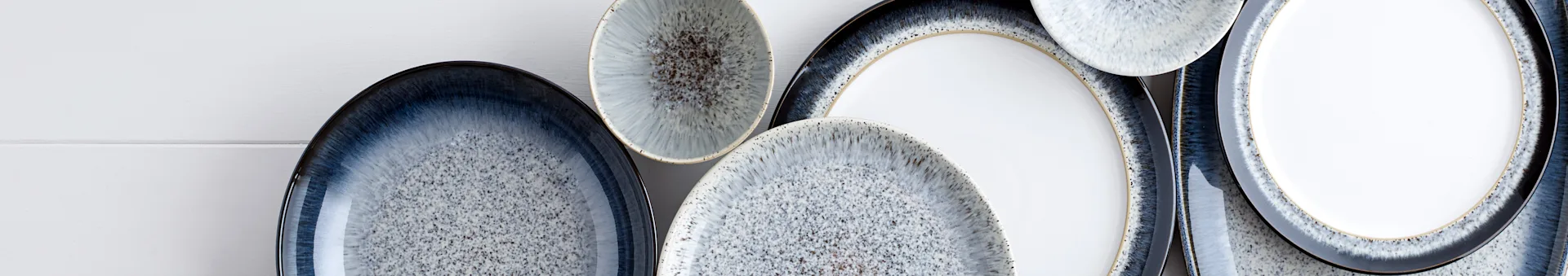 Assortment of ceramic plates and bowls with speckled blue, grey, and white reactive glaze and dark rims.