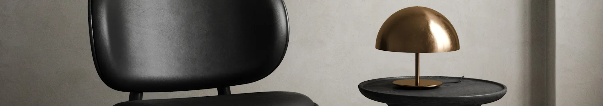 A close-up of a black leather chair next to a dark wooden side table with a dome-shaped brass table lamp.