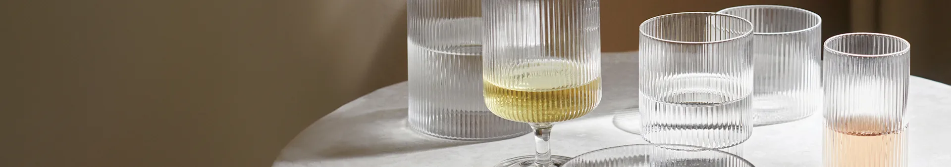 Ribbed glass champagne flute with yellow liquid next to three ribbed glass cups with clear and pink liquid on a light table.