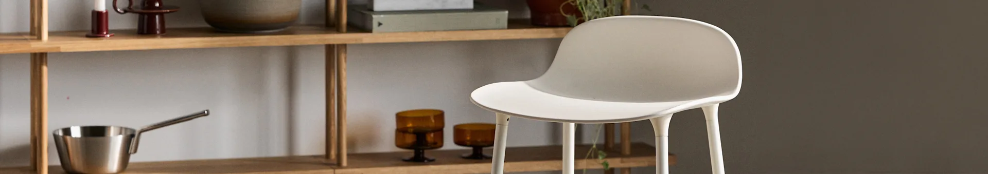 A light-colored bar stool with a curved seat and backrest, positioned in front of a wooden shelving unit with decorative items.