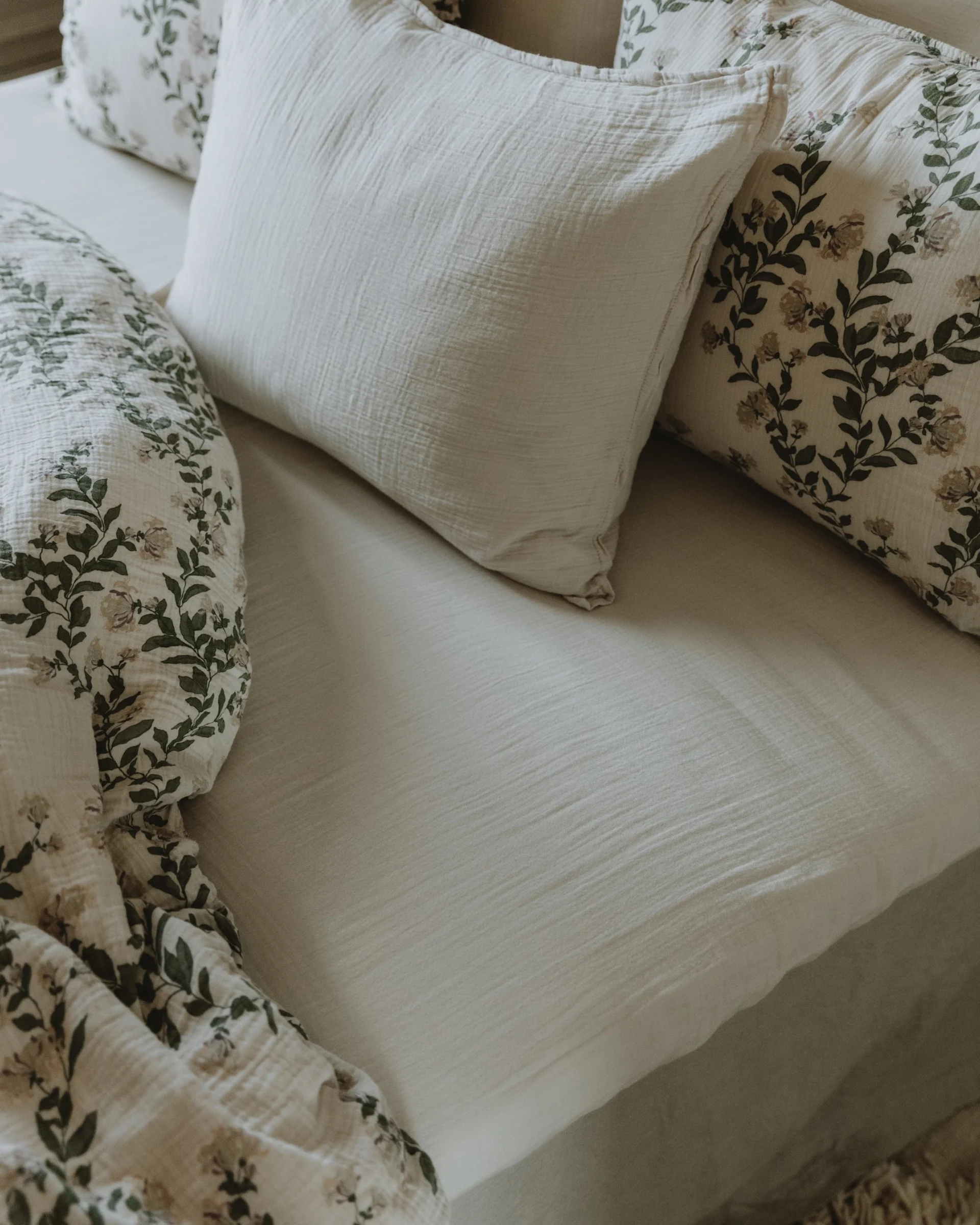 Light beige bed with soft, textured plain sheets and floral pillows with green leaves.