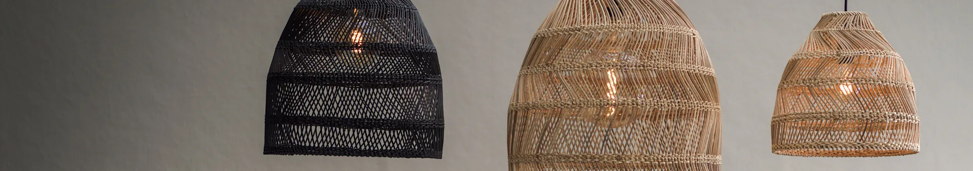Three woven pendant lights hanging. One black, two natural rattan, all with exposed bulbs.