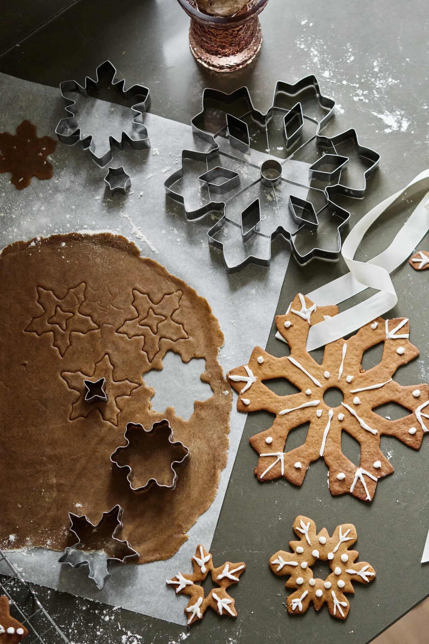 Gingerbread snowflake cookies baking: dough, metal cutters, and iced cookies on a grey surface.