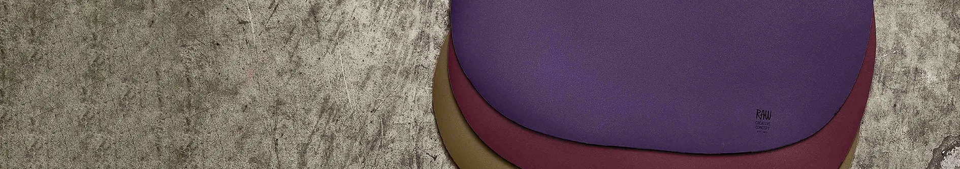 Three curved leather samples in purple, burgundy, and tan, layered on a concrete surface, with a 'RAW CREATIVE CONCEPT' logo on the purple piece.