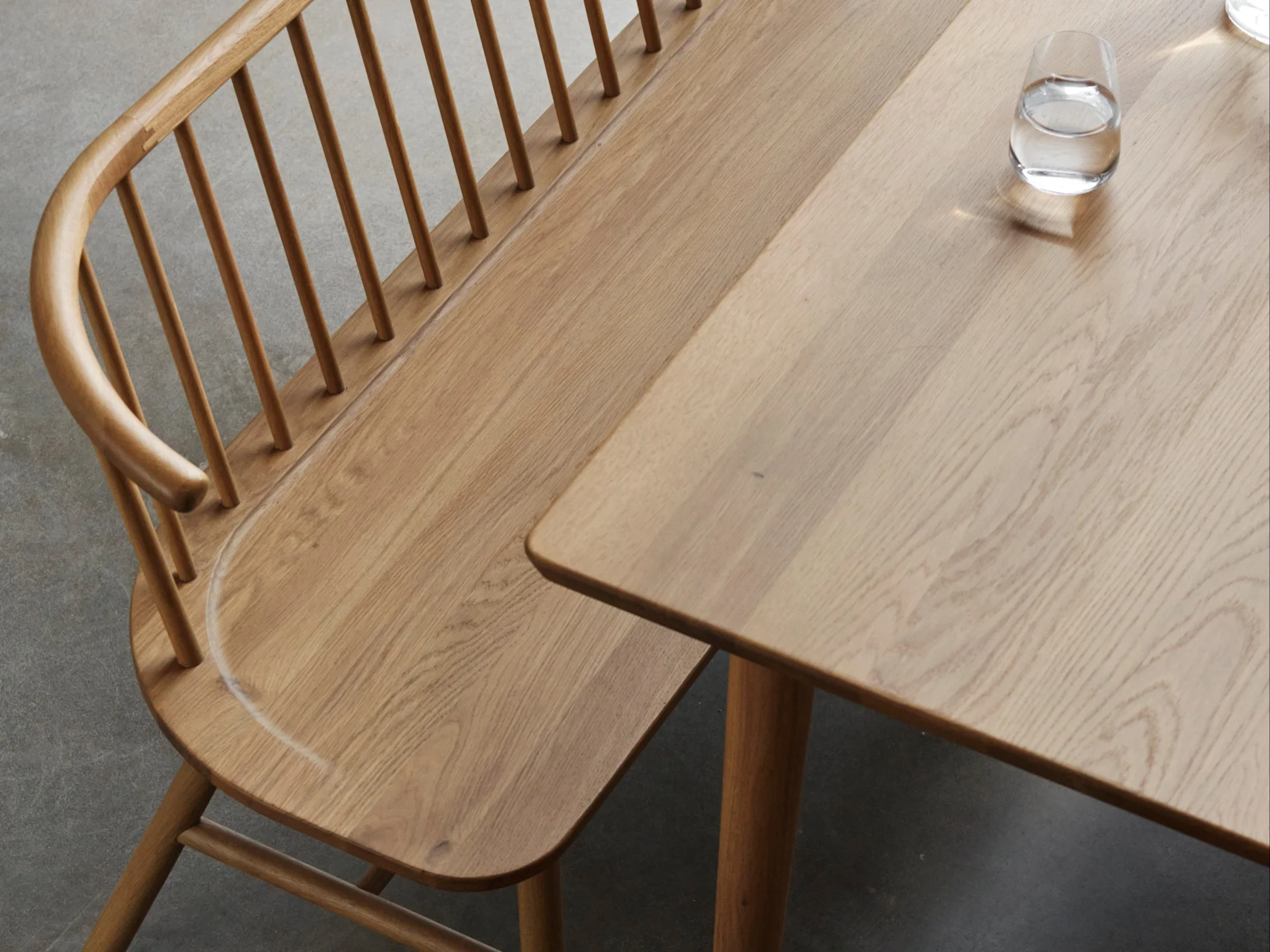 Light oak wooden bench with a slatted backrest and a matching table with a glass of water on a gray floor.