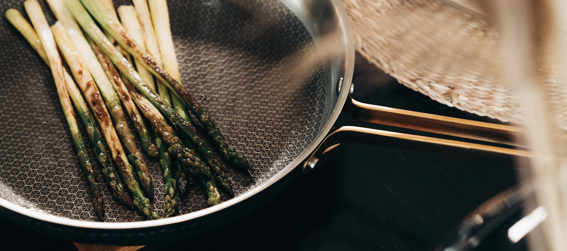 Asparagus spears cooking in a textured pan with a golden handle, seen from above.