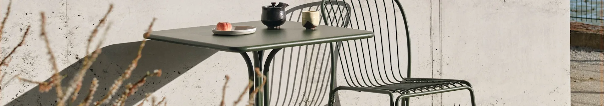 Dark green outdoor table and chair in sunlight, with a peach and ceramic ware on the table.