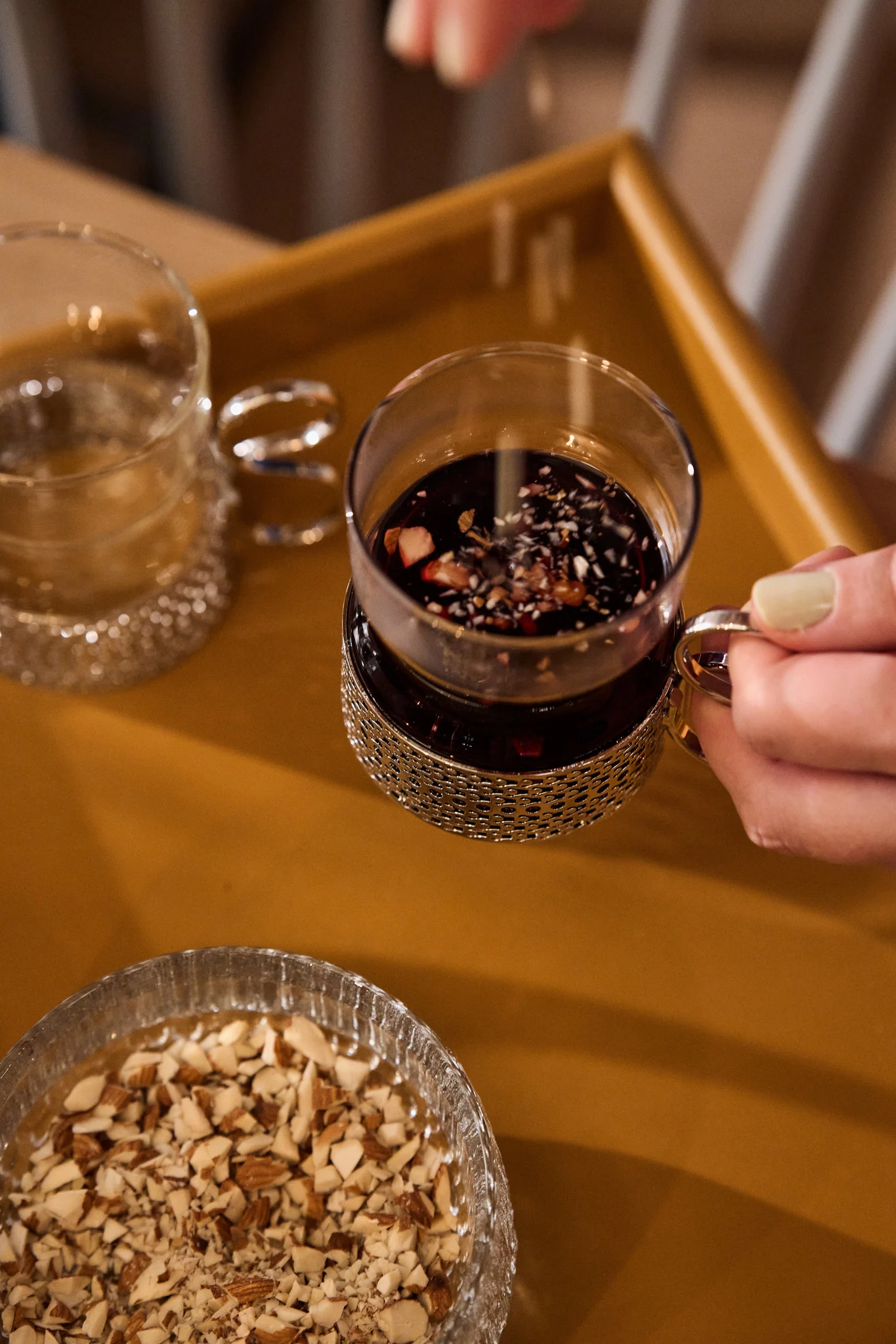 Swedish mulled wine, glögg, is an integral part of Christmas in Sweden. Here, a hand holds a cup of glögg and sprinkles chopped almonds into it.