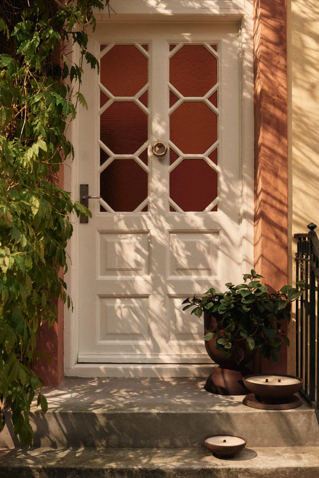 White front door with octagonal glass panels, green vines on left, and a planter with two candles on the steps.
