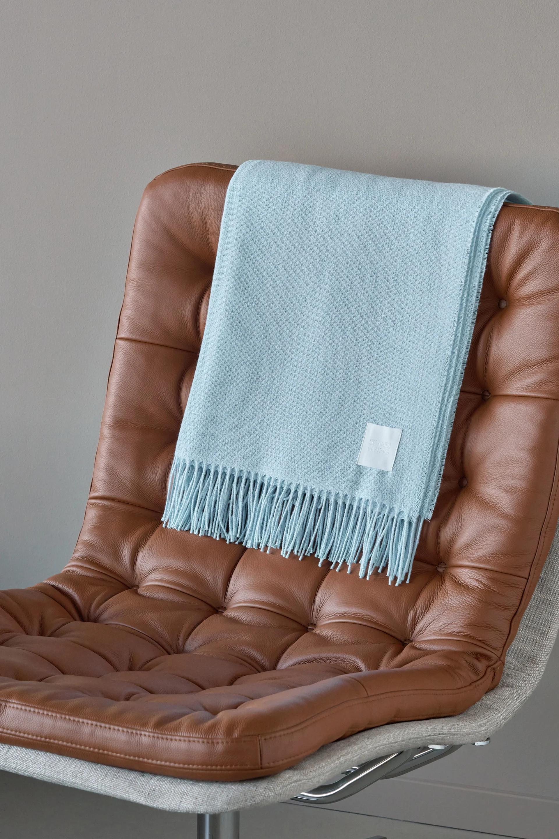 Light blue fringed blanket draped over a brown tufted leather armchair.