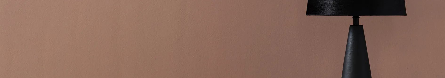 A black table lamp with a textured shade against a reddish-brown textured wall.