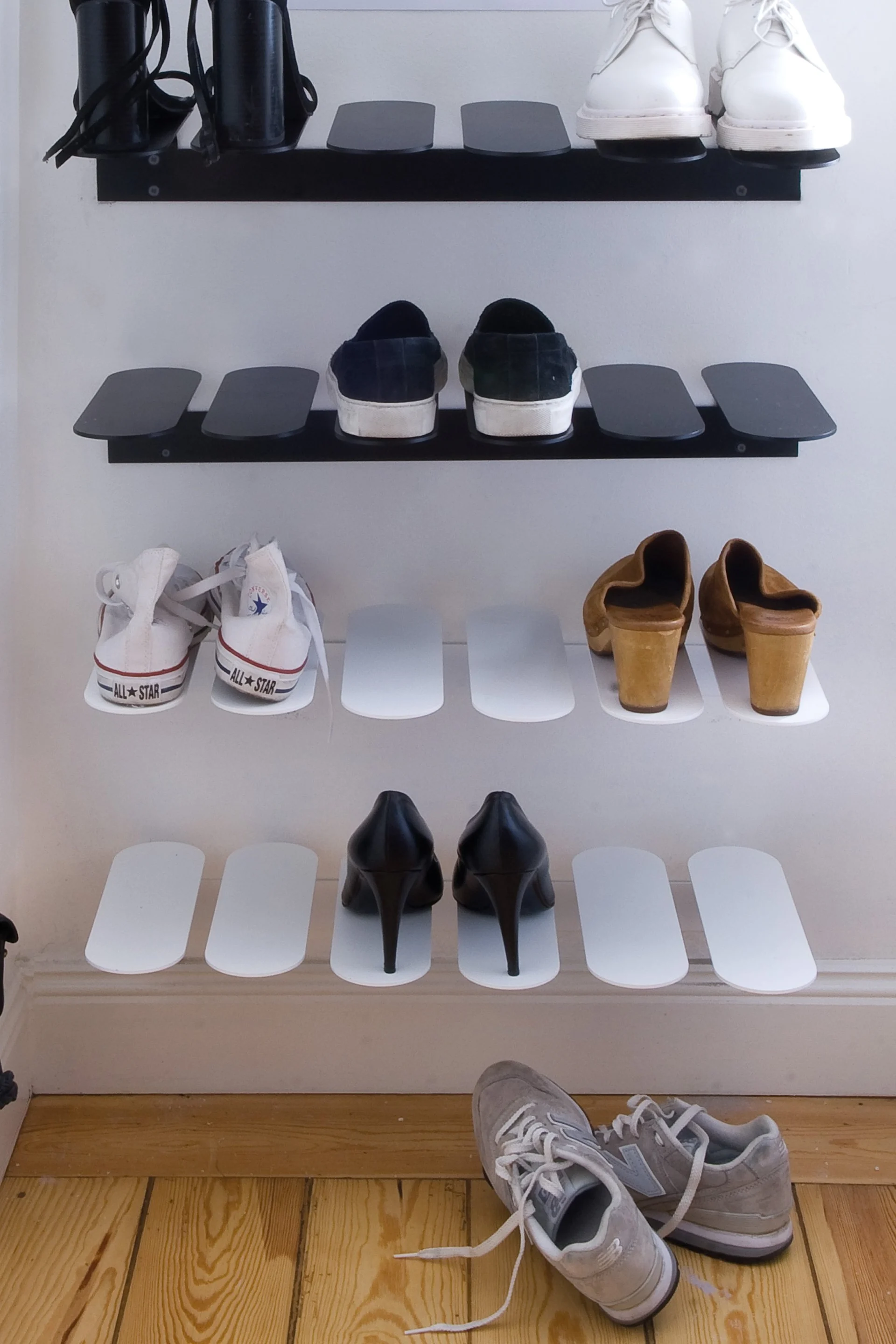 Various shoes displayed on wall-mounted shelves, including black heels, white sneakers, dark slip-ons, clogs, and grey sneakers.