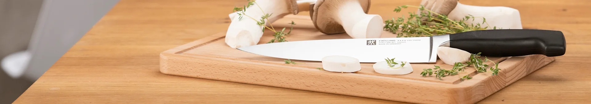 ZWILLING knife on a wooden cutting board with large white mushrooms and fresh thyme.