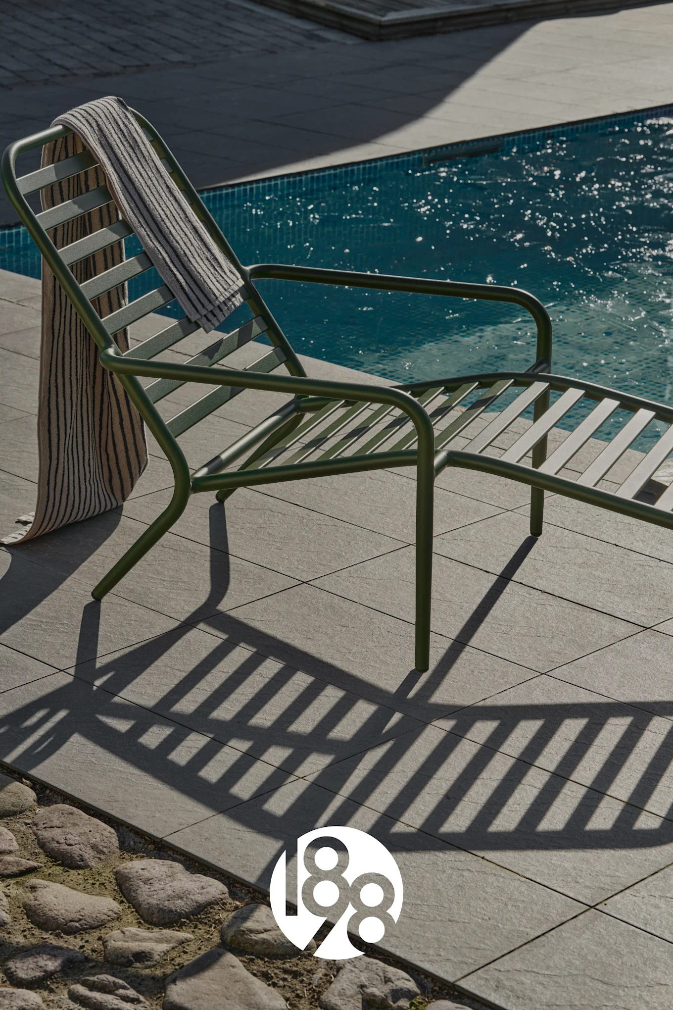 Dark green lounge chair with a striped towel next to a blue swimming pool.
