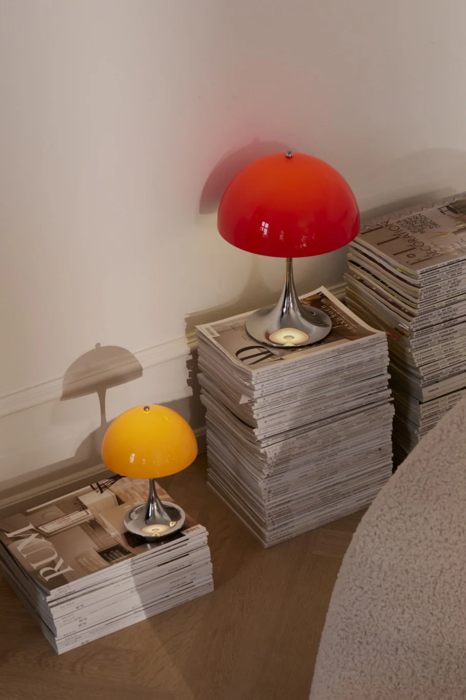 Red and yellow mushroom lamps with chrome bases, sitting on stacks of magazines.