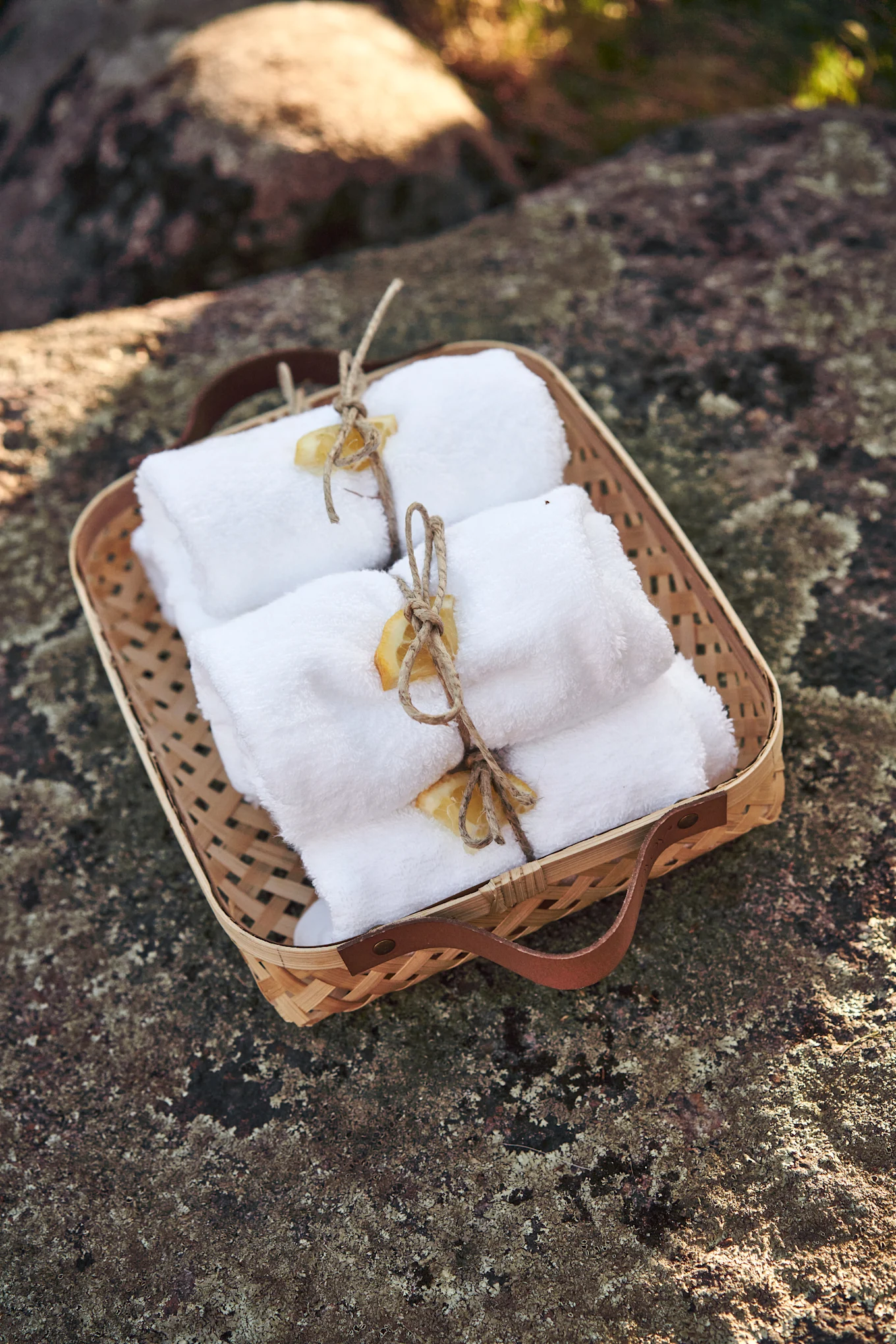 Woven basket holding rolled white towels tied with twine and dried citrus slices on a textured rock.