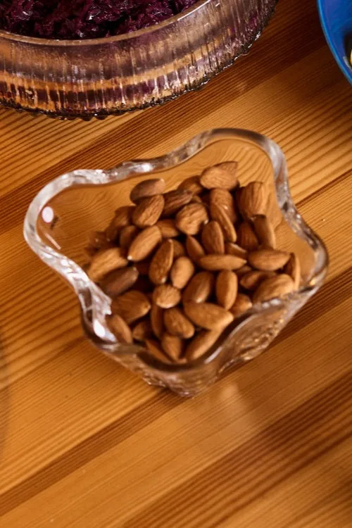 Heart-shaped glass bowl filled with whole almonds on a wooden table.