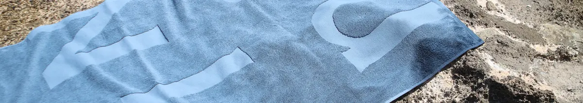 A blue towel with a lighter blue wavy pattern, laid on a rocky surface.
