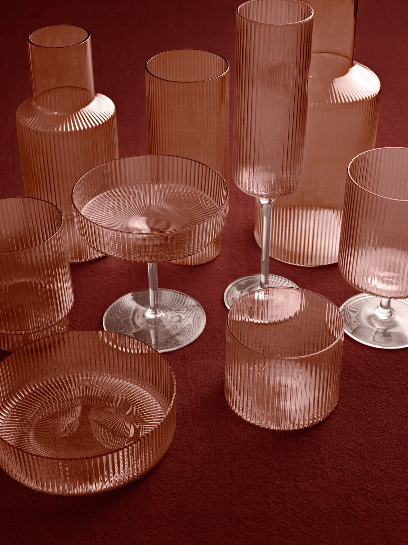 Collection of ribbed, reddish-brown glass vases, tumblers, and stemmed bowls on a deep red surface.