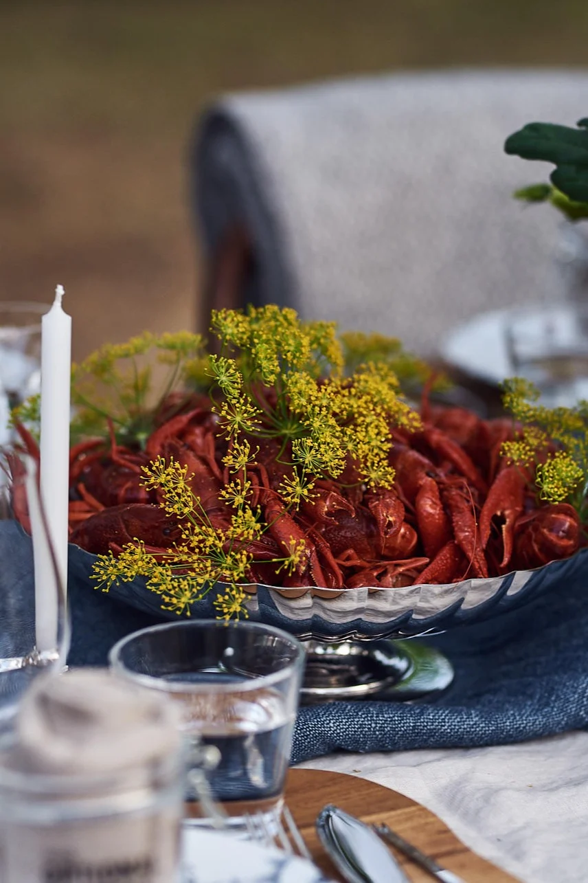 Outdoor table set with a silver bowl of red crawfish and dill, candles, and a flower arrangement.