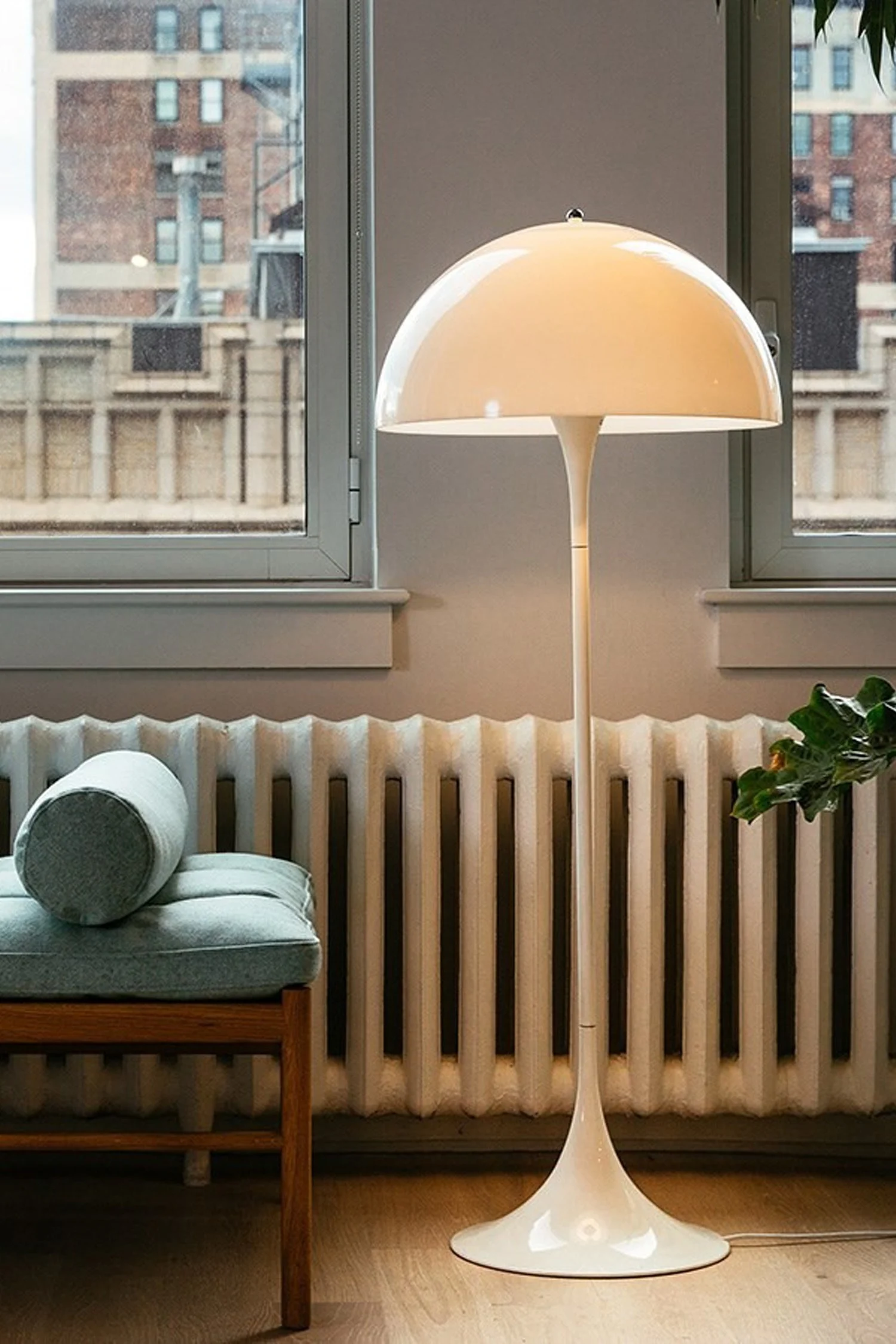 Cream mushroom-shaped floor lamp next to a blue bench and a white radiator by a window.