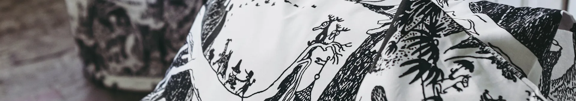 White fabric with whimsical black illustrations of antlered creatures, figures, and stylized trees.
