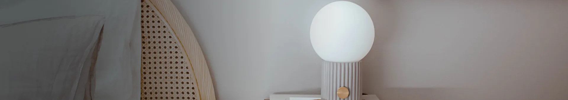 Modern table lamp with an oval white shade, ribbed light grey base, and a round brass accent, next to a rattan screen.