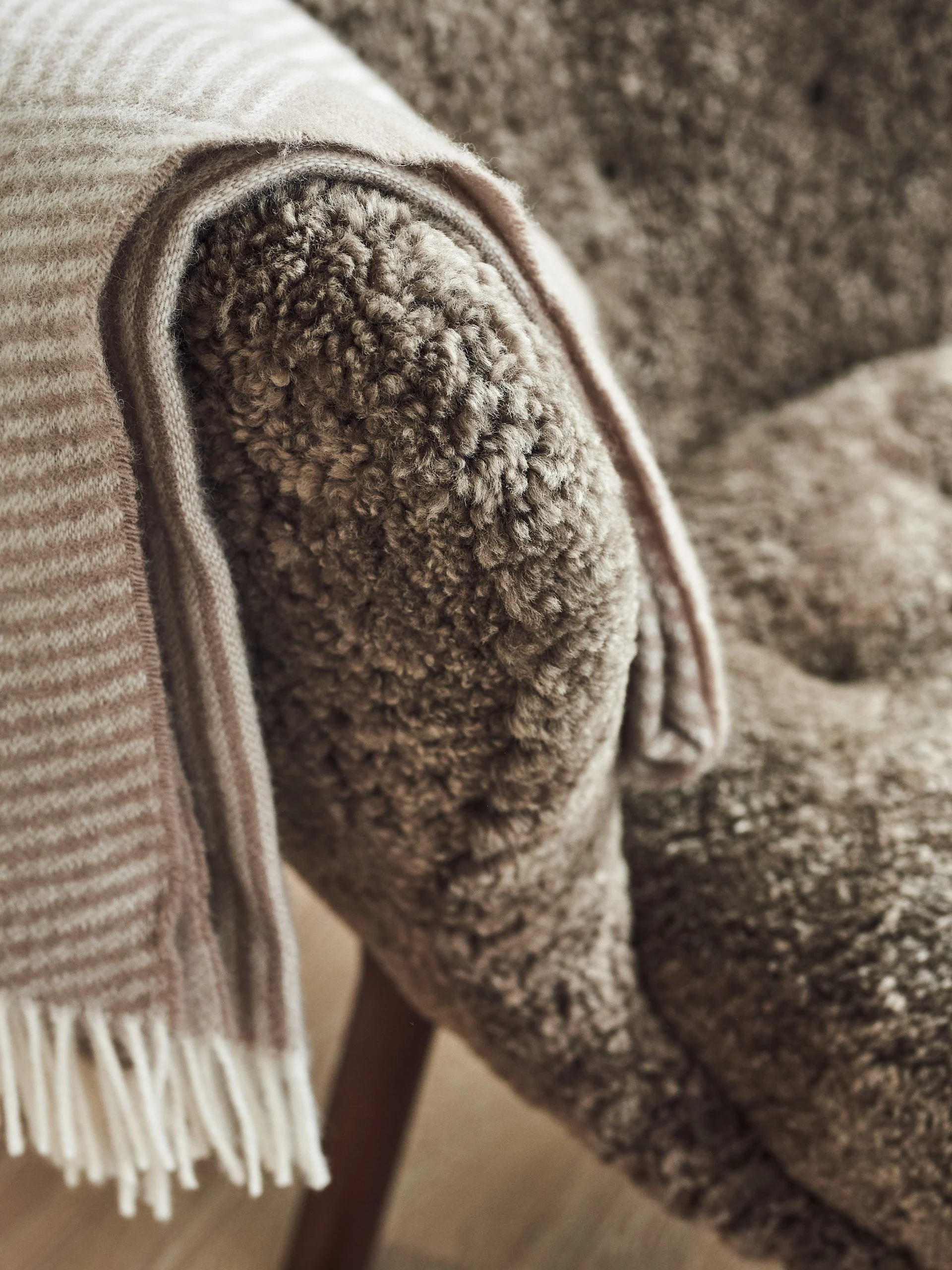 Close-up of a light brown curly-textured chair with a striped beige and white blanket draped over its arm.