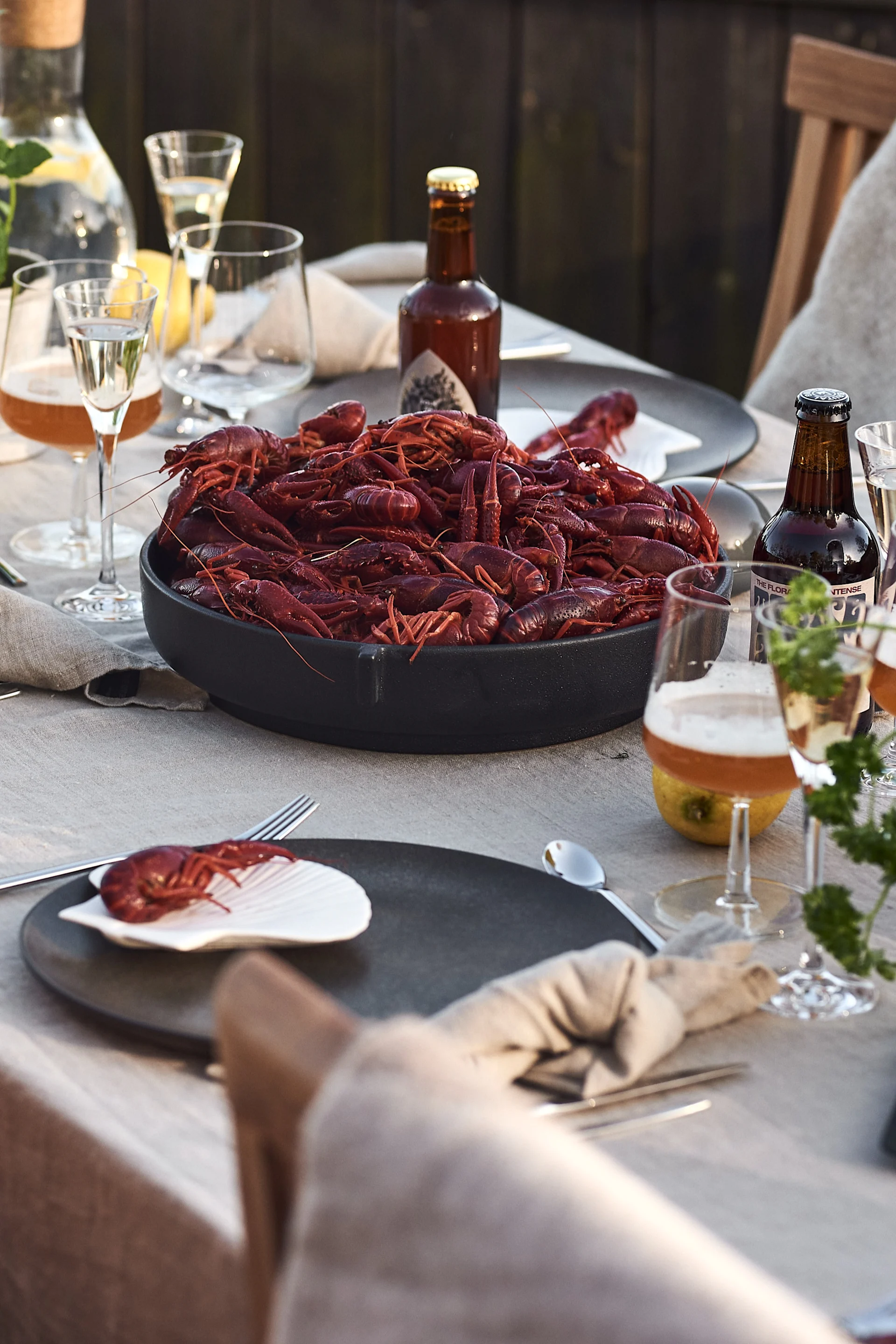 Outdoor table set with a large bowl of cooked red crayfish, individual crayfish on a shell, beer, wine, and water.