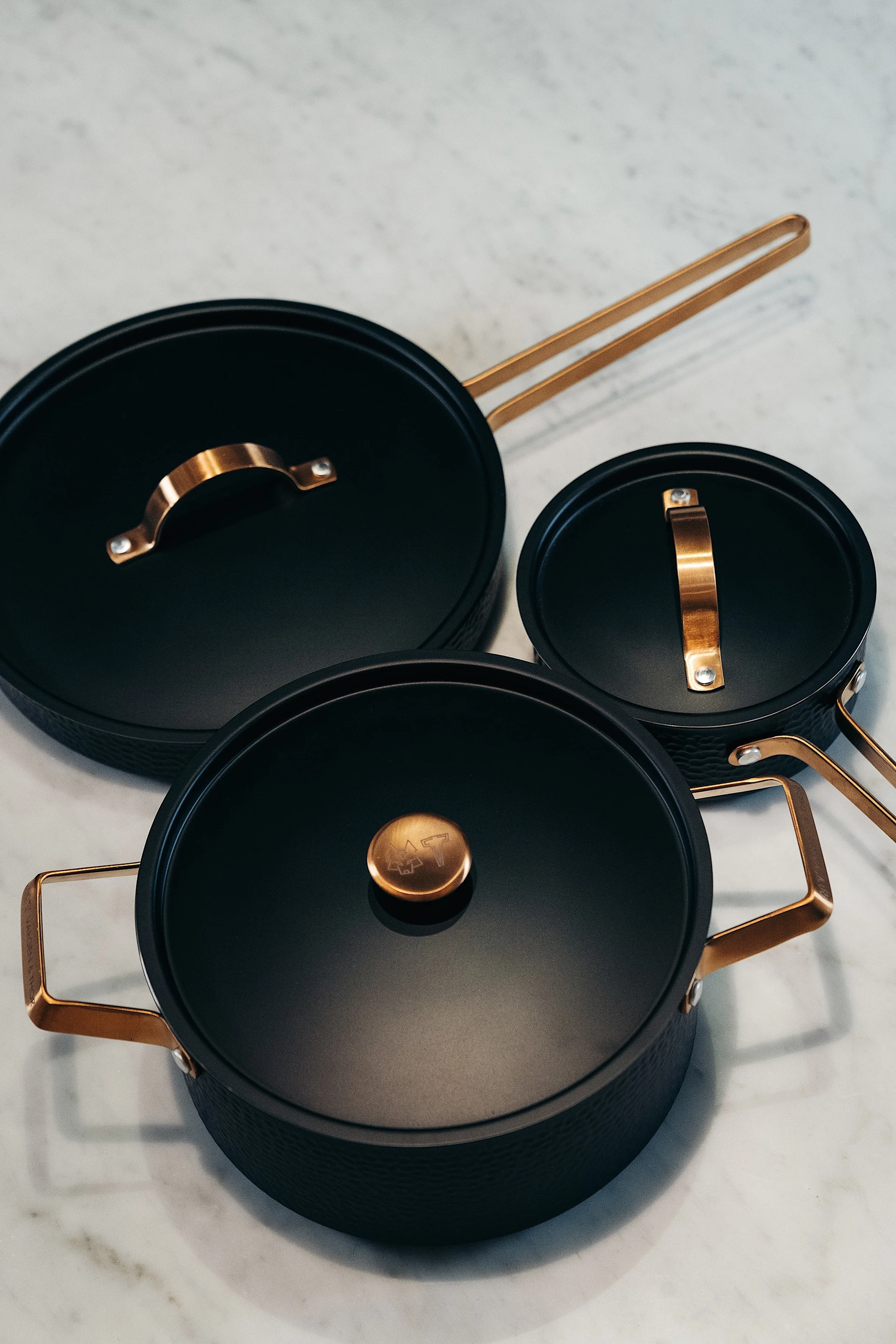 Three black pots and pans with bronze handles on a marble surface.