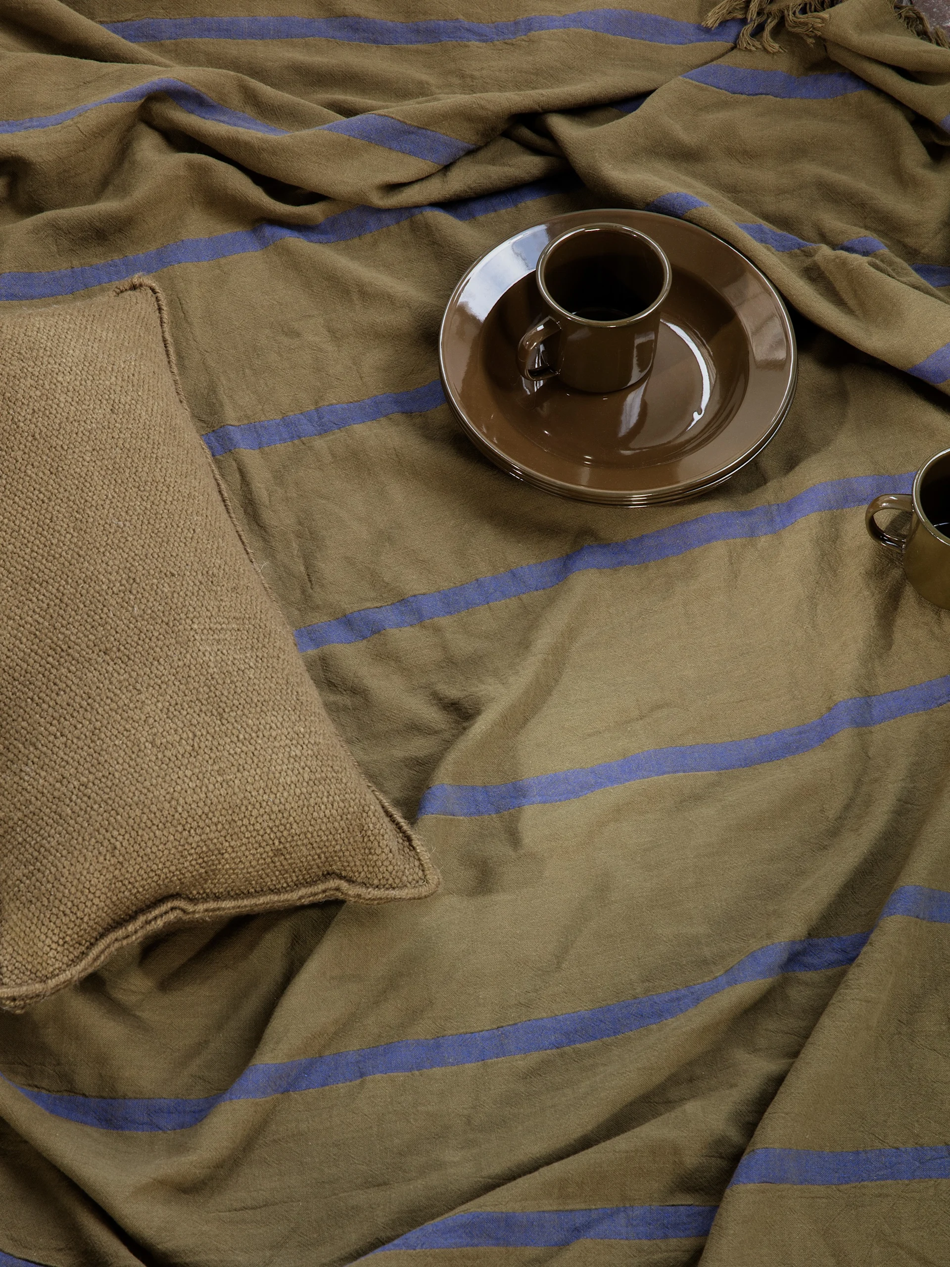 Brown striped blanket with a woven beige pillow and two brown ceramic cups.