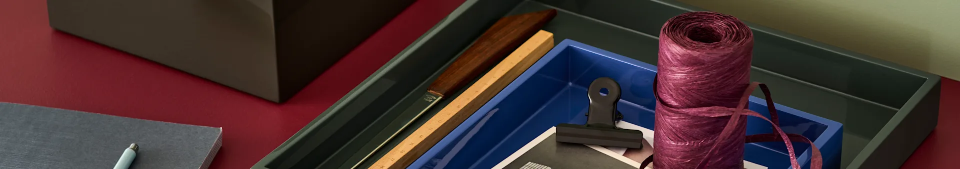 Desk accessories: dark green and blue trays, purple ribbon, a ruler, black clip, and grey notebook with a pen.