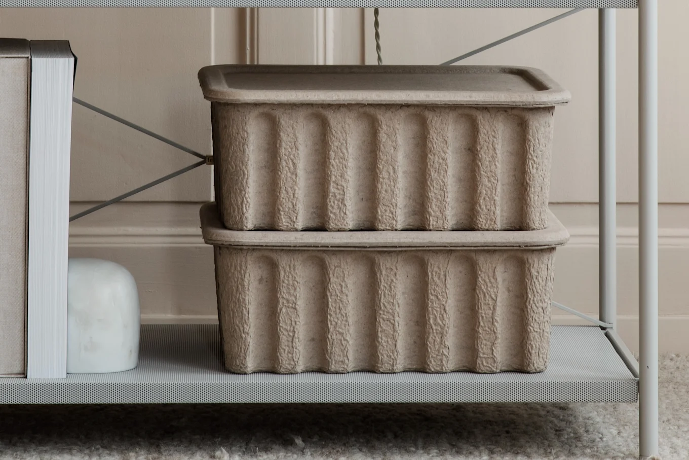 Two stacked, textured, light brown storage boxes with lids on a gray perforated shelf.