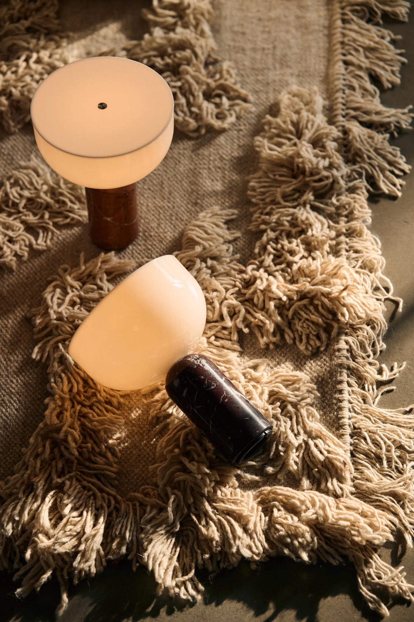 Two illuminated lamps with frosted glass shades and marble bases on a shaggy, fringed rug.