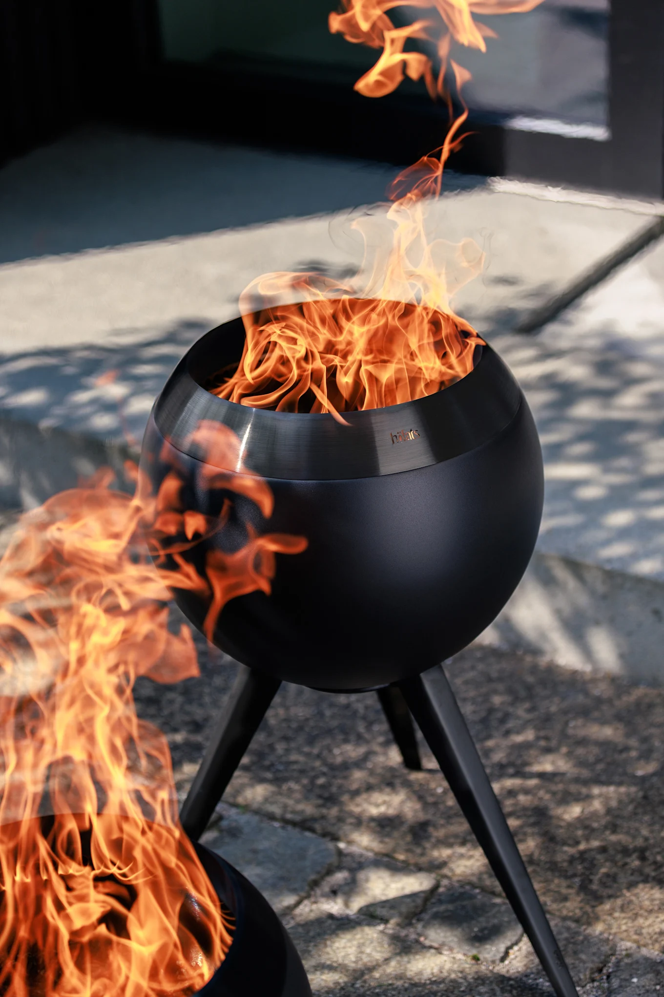 Two black spherical outdoor fire pits with bright orange flames on a paved patio.