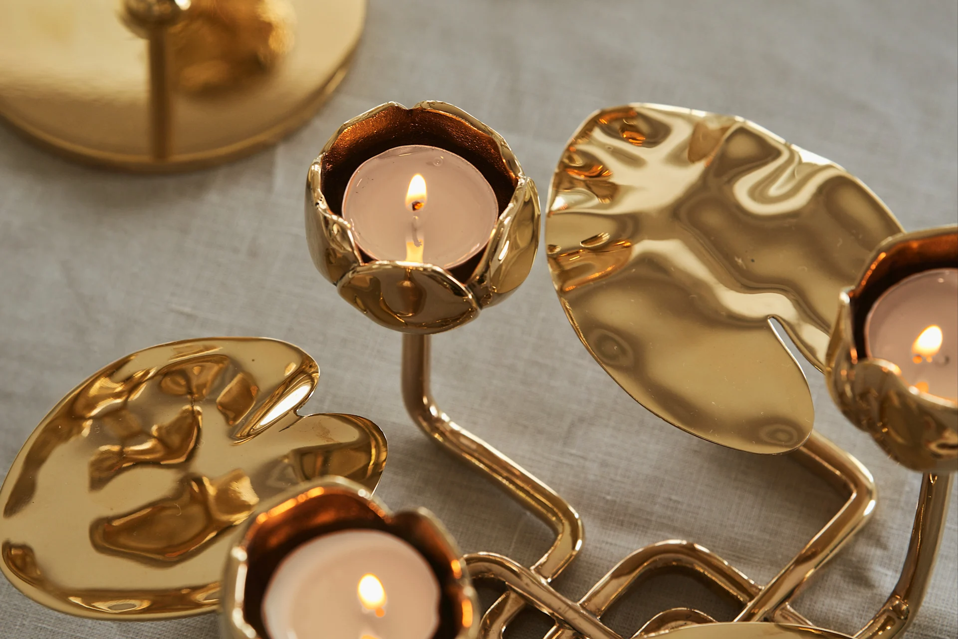Golden candelabra with lit tea lights and lily pad-shaped bases on a linen tablecloth.
