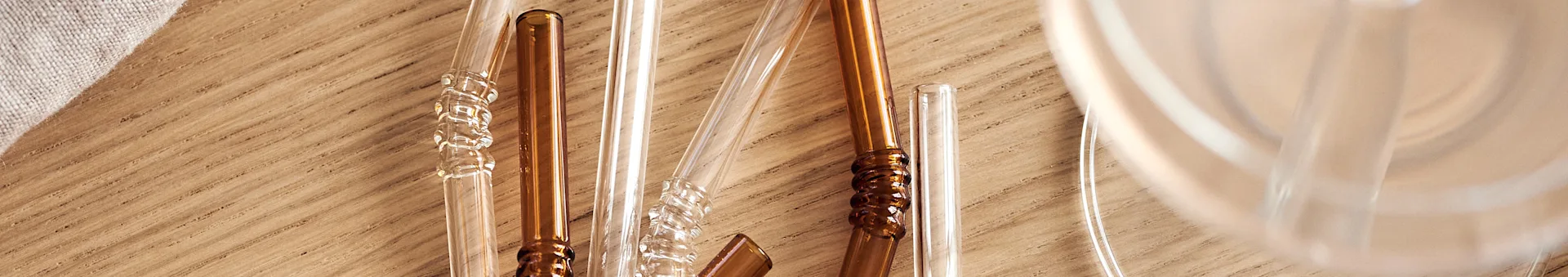 Clear and amber glass straws with textured details on a wooden surface.