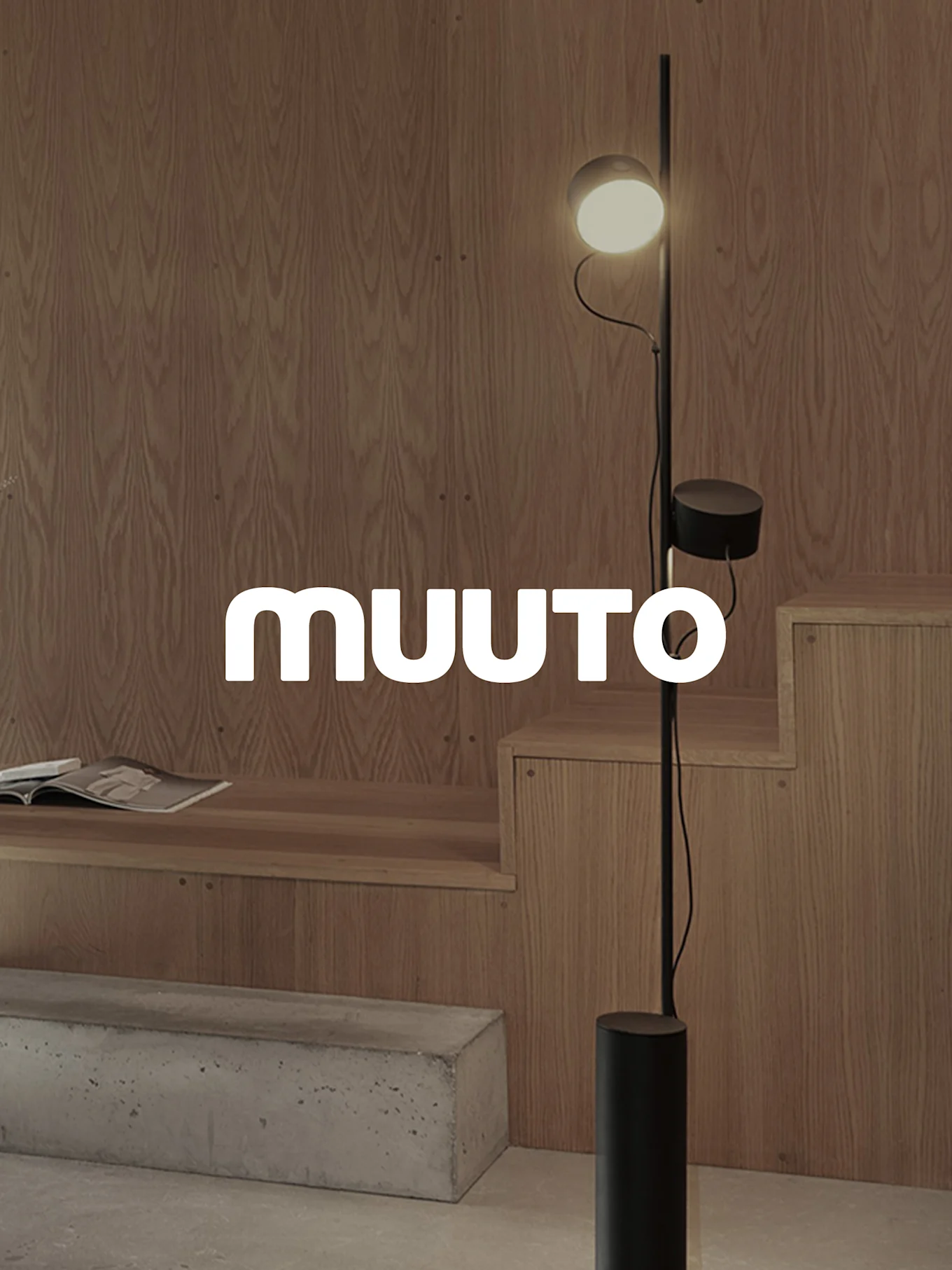 A modern black floor lamp with two lights in a room with wood paneling and a concrete bench, with the 'MUUTO' logo.