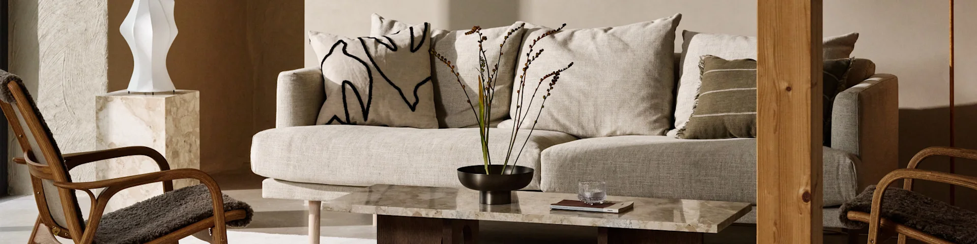 A modern living room featuring a light fabric sofa with decorative pillows, a marble coffee table, and wooden chairs with dark cushions.