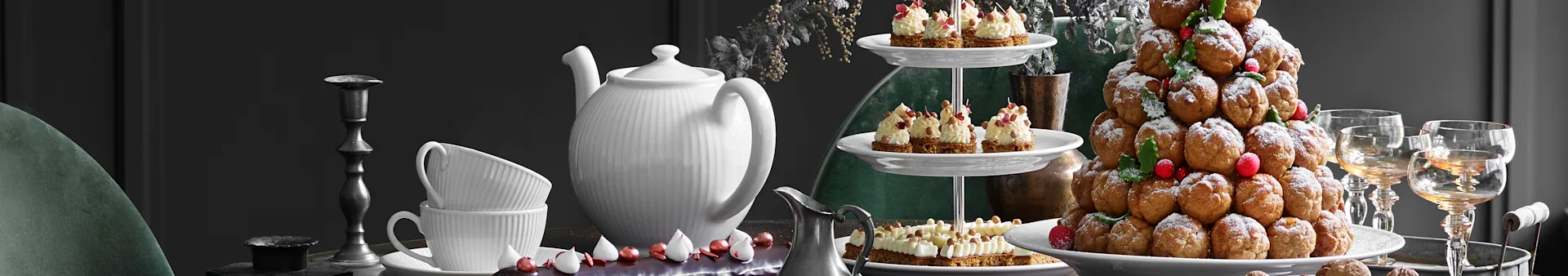 A festive dessert table with a white teapot, teacups, tiered stand with tarts, and a sugar-dusted profiterole tower.