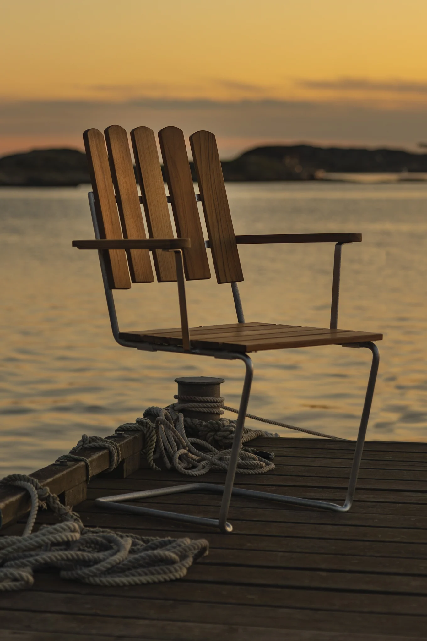 Wooden chair on a dock at sunset with water and faint land in the background.
