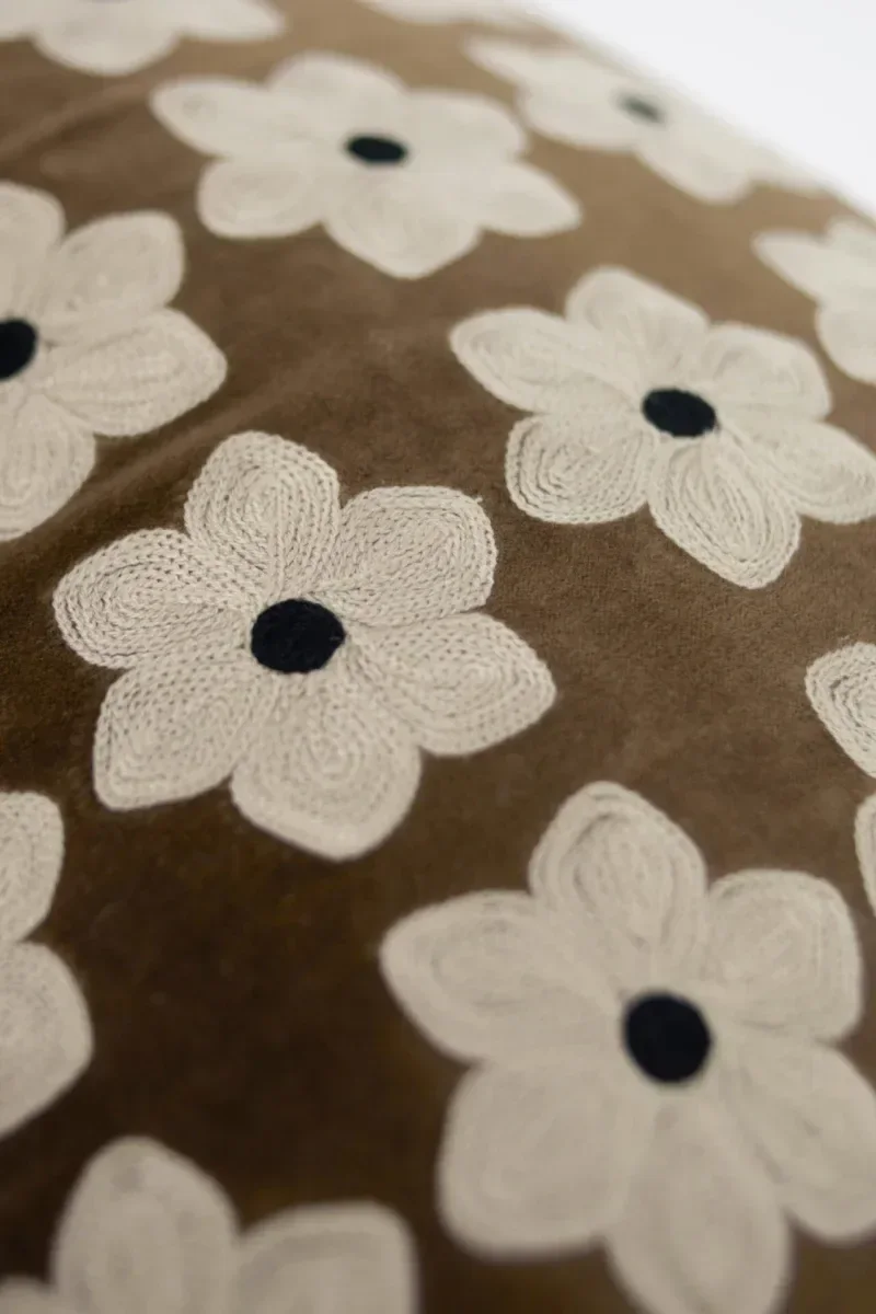 A brown cushion embroidered with white flowers that reflects the interior design trends of 2026.