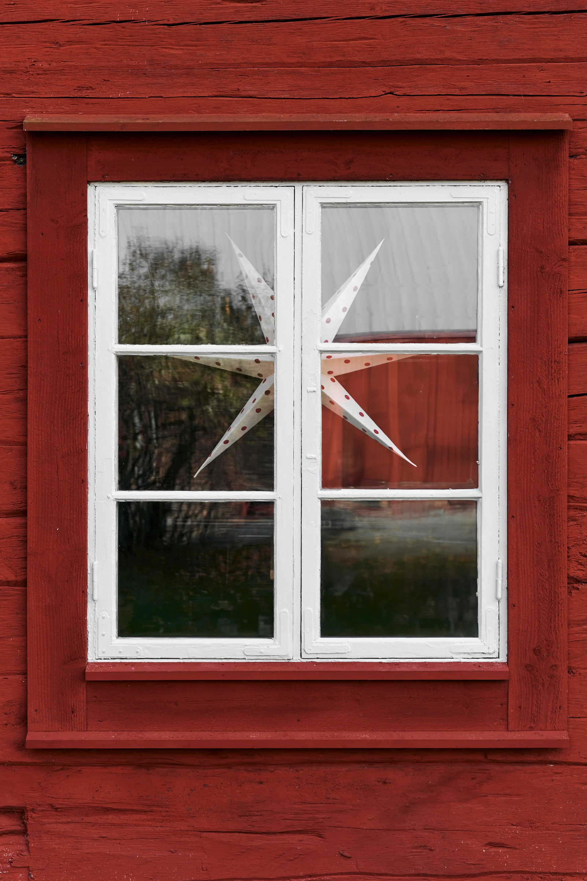 White window with a white and red polka-dotted star decoration, set in a rustic red wooden wall.