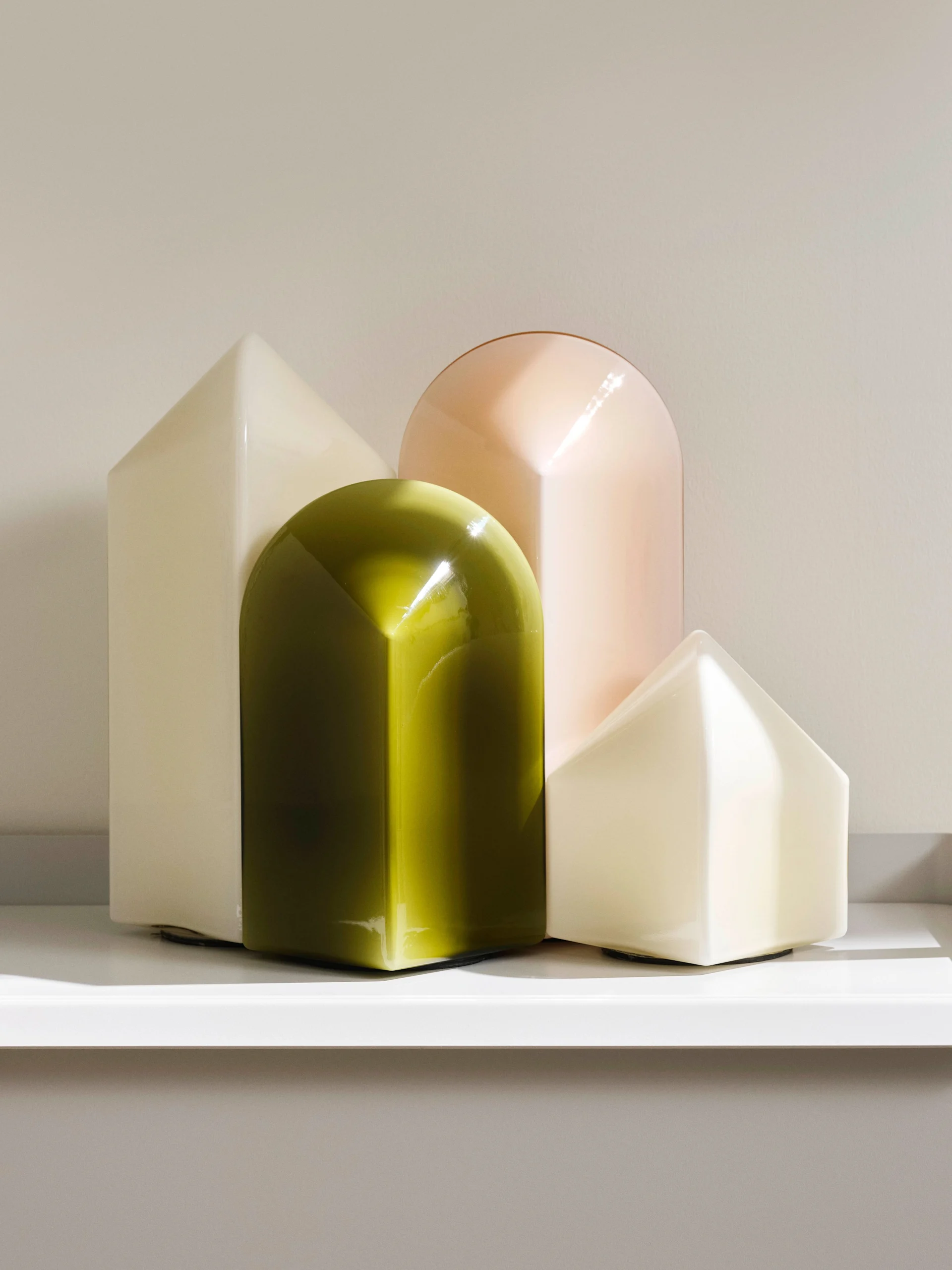 Four translucent, geometric decorative objects: two cream house shapes, an olive green arch, and a peach arch.